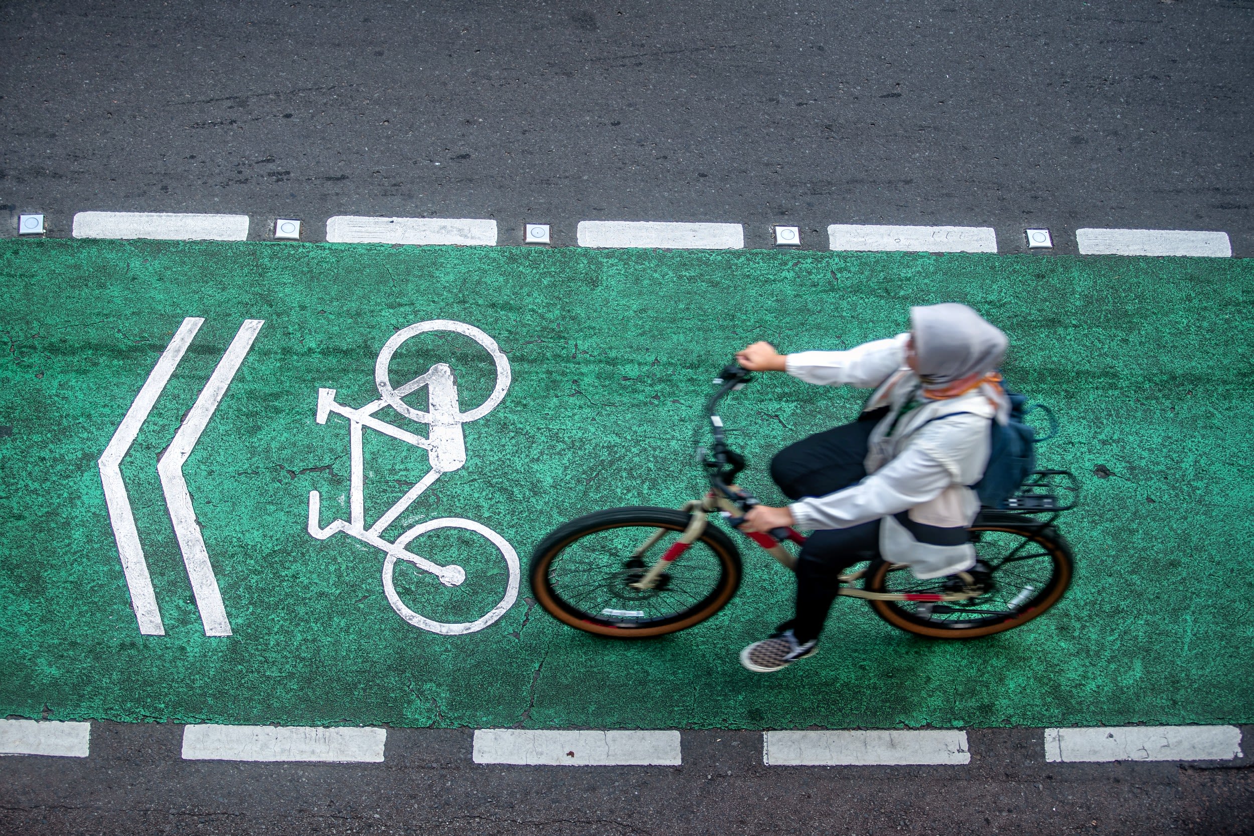 Overhead view of a woman in a headscarf riding a bike in a green bike lane in Jakarta